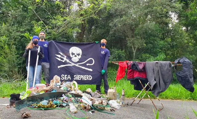 Voluntários na frente de pilha de lixo segurando bandeira da Sea Shepherd
