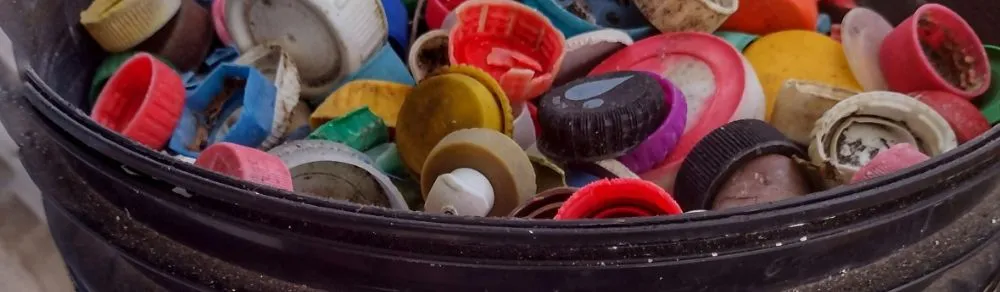 Balde cheio de tampinhas plásticas coloridas recolhidas em um mutirão de limpeza