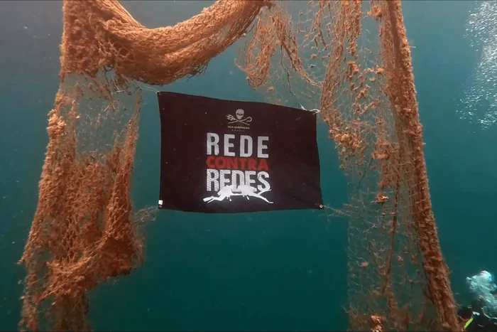 Bandeira Rede Contra Redes estendida sobre uma grande rede fantasma submersa