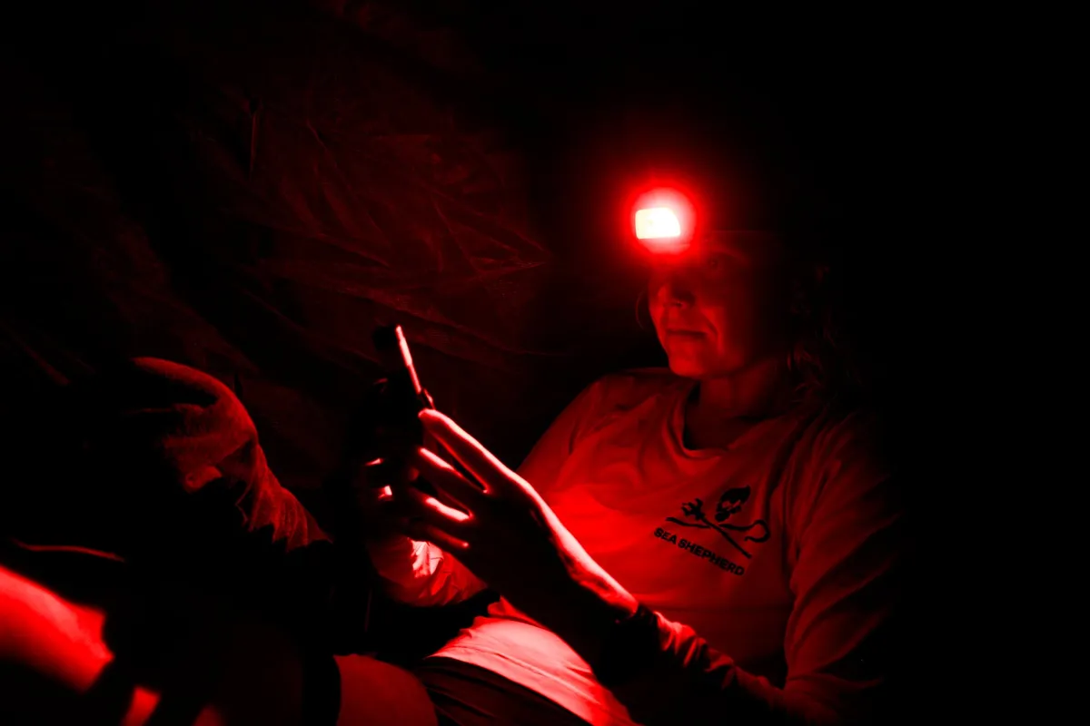 Integrante da equipe trabalhando à noite sob a luz vermelha de uma lanterna de cabeça