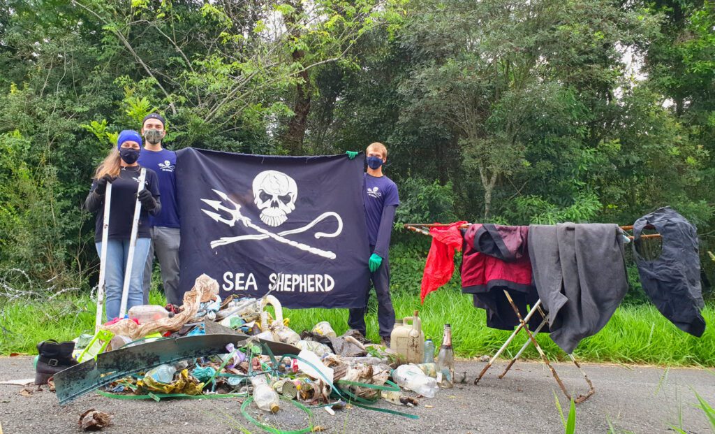 Voluntários na frente de pilha de lixo segurando bandeira da Sea Shepherd