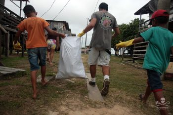 Criança e voluntário da Sea Shepherd carregando saco de lixo no Amazonas